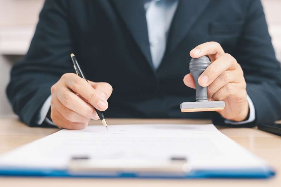 Un professionnel en costume signe et tamponne un contrat de mutuelle d'entreprise sur un bureau.