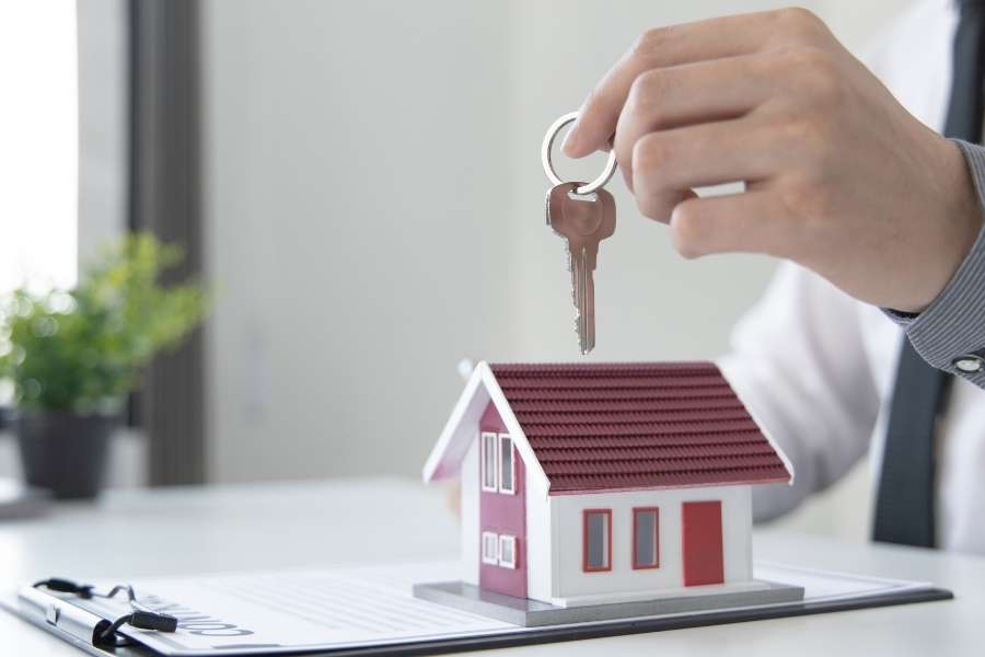 Un professionnel tient une clé au-dessus d'une maison miniature pour symboliser la souscription à une assurance habitation.